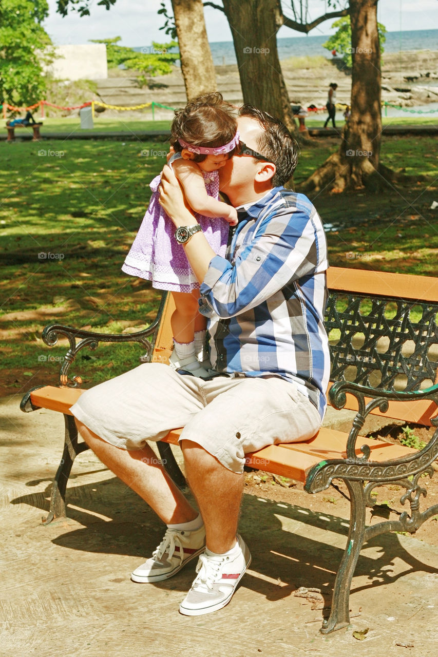 a father holds and kisses his baby with a muted tropical setting in