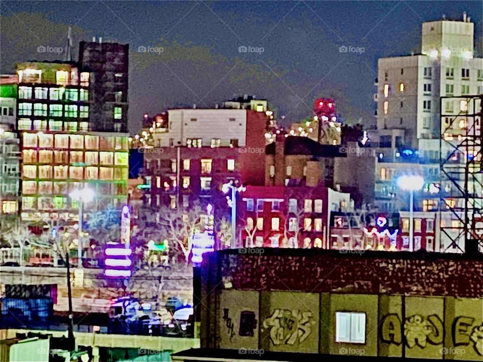A late night view fr the “Greenpoint”, Bklyn side of the “Pulaski Bridge” towards LIC w illuminated buildings of multiple heights. The street lights & electric lights in the buildings are enough to show the various colors. 2022. Hypnotic Productions