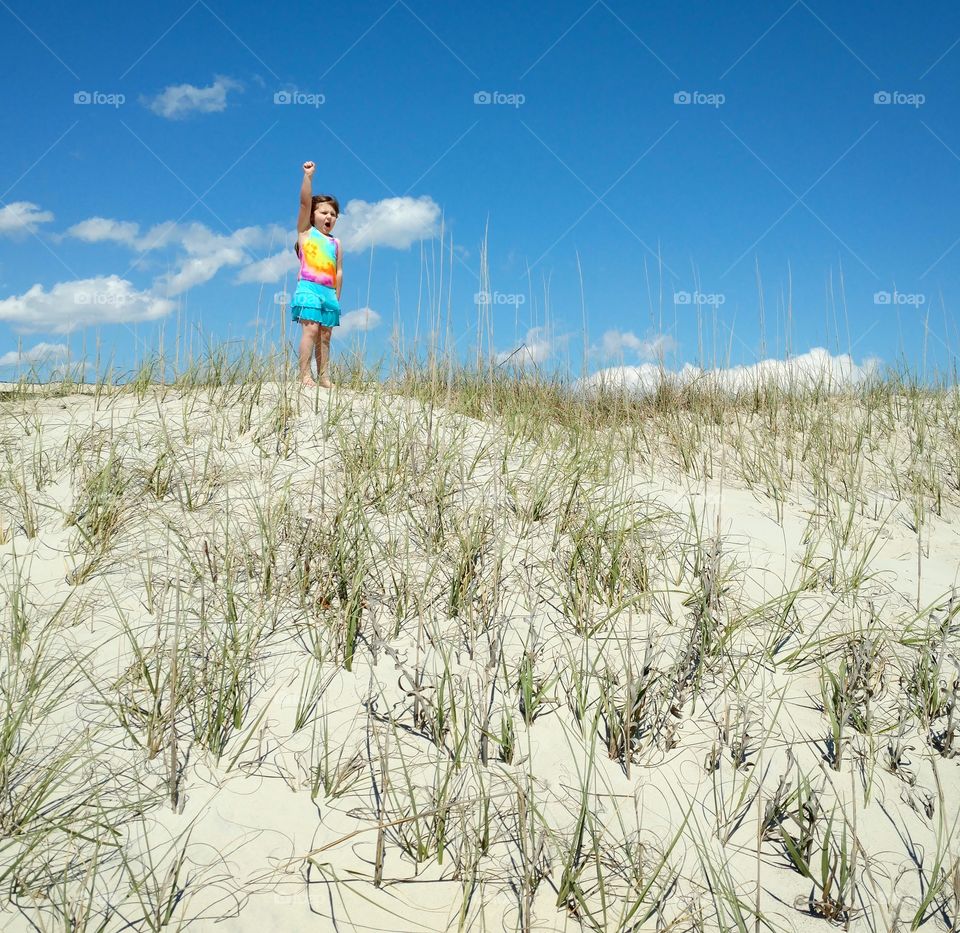 A young girl celebrating after climbing to the top of a sand dune on a beautiful, sunny day
