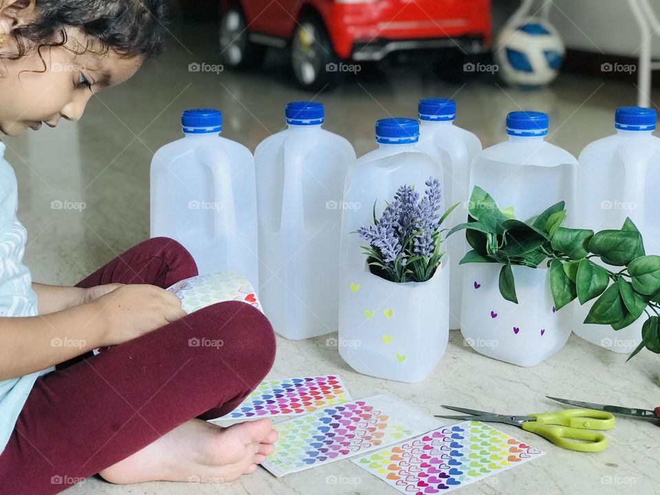 A four year old girl doing craft and making flower pots from leftover plastic milk bottles.teaching kids about reuse things and how to save environment.