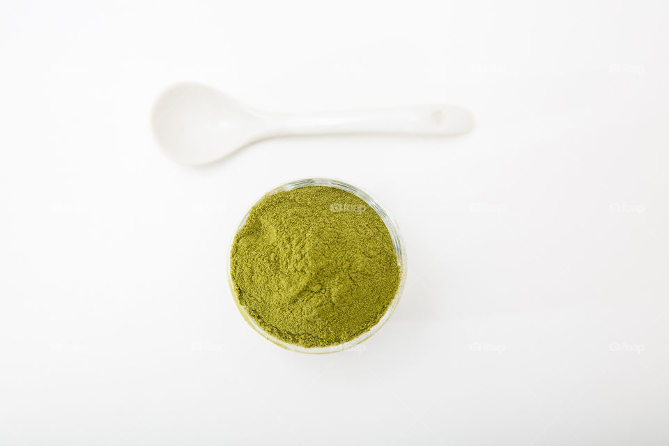 Product wheat grass powder in white bowl with white spoon isolated on pure white background. Image from top.