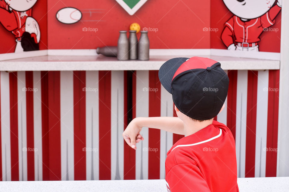 Young boy wearing white and red playing a carnival toss game outdoors against a white and red background