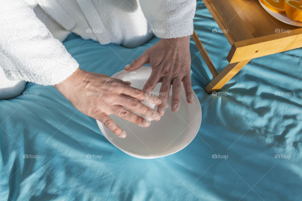 A man at home takes care of himself and does a manicure at home on a blue background and with orange.