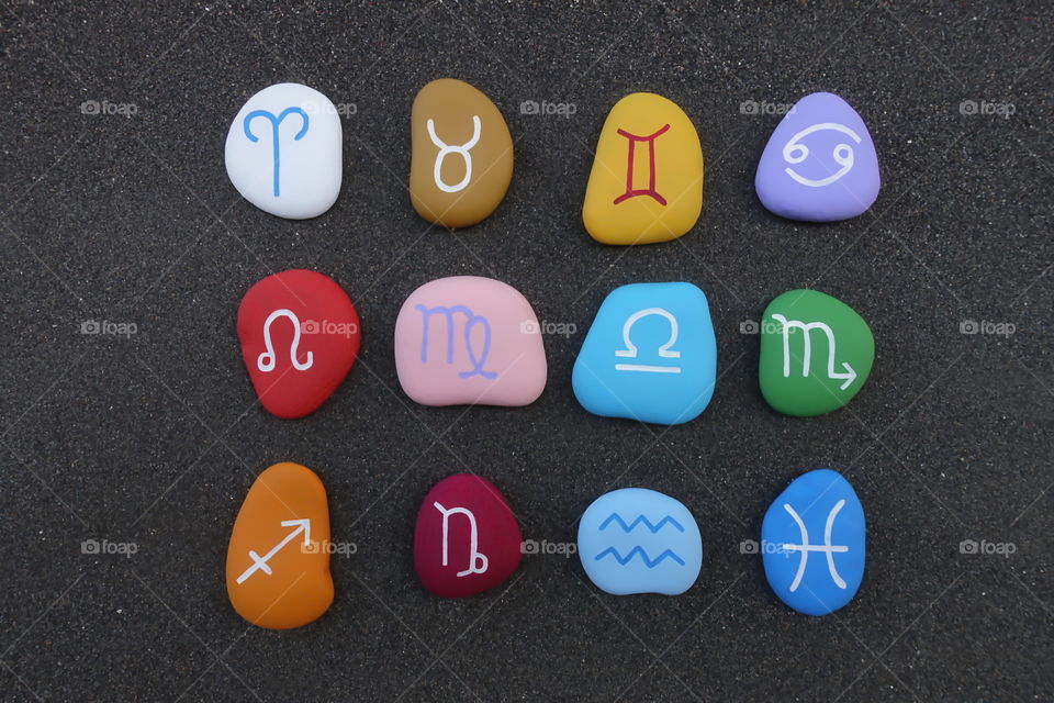 Astrological signs with colored and graved stones over black volcanic sand