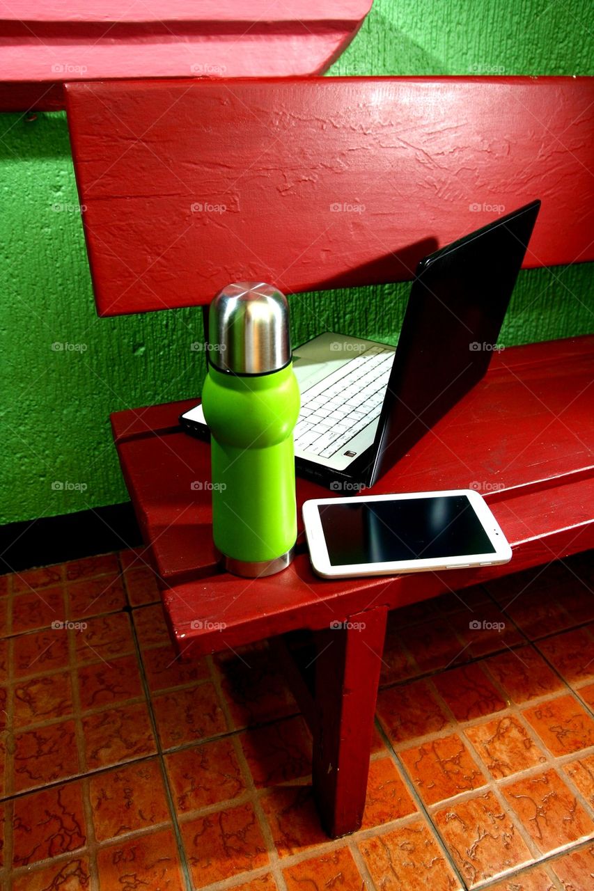 flask, tablet and laptop computer on an outdoor bench