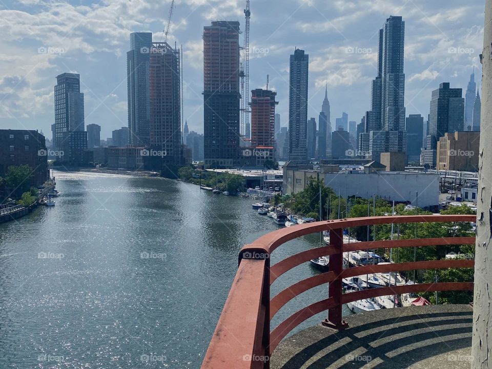The curved red metal railing around the central outpost of the “Pulaski Bridge” at “Newtown Creek” protects onlookers from stepping too far and it gives the panoramic view of NYC a more rounded appearance. 2023. Hypnotic Productions