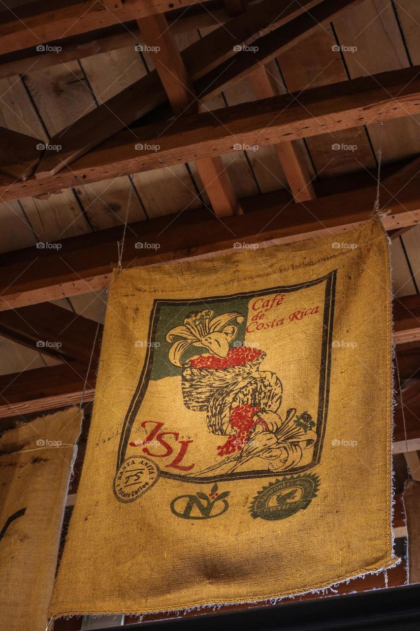 Various coffee bean sacks used as decor in a coffee shop with exposed wood beams on the ceiling 