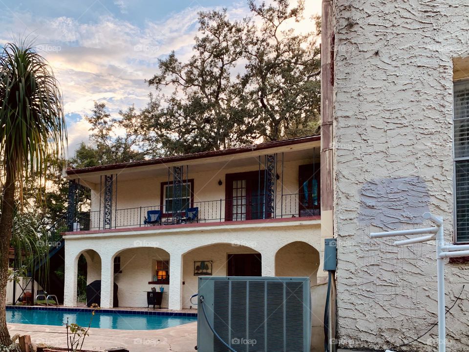 Gated white and red spanish old style architecture residential large house built in the early 1900s. Charming pretty style and beautiful landscaping with pool and chairs with great setting in a tropical environment with arched openings in patio area.