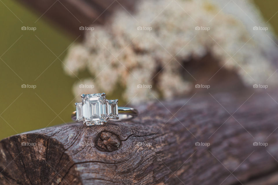 A wedding ring sits on top of a wooden bench with flowers after an engagement 