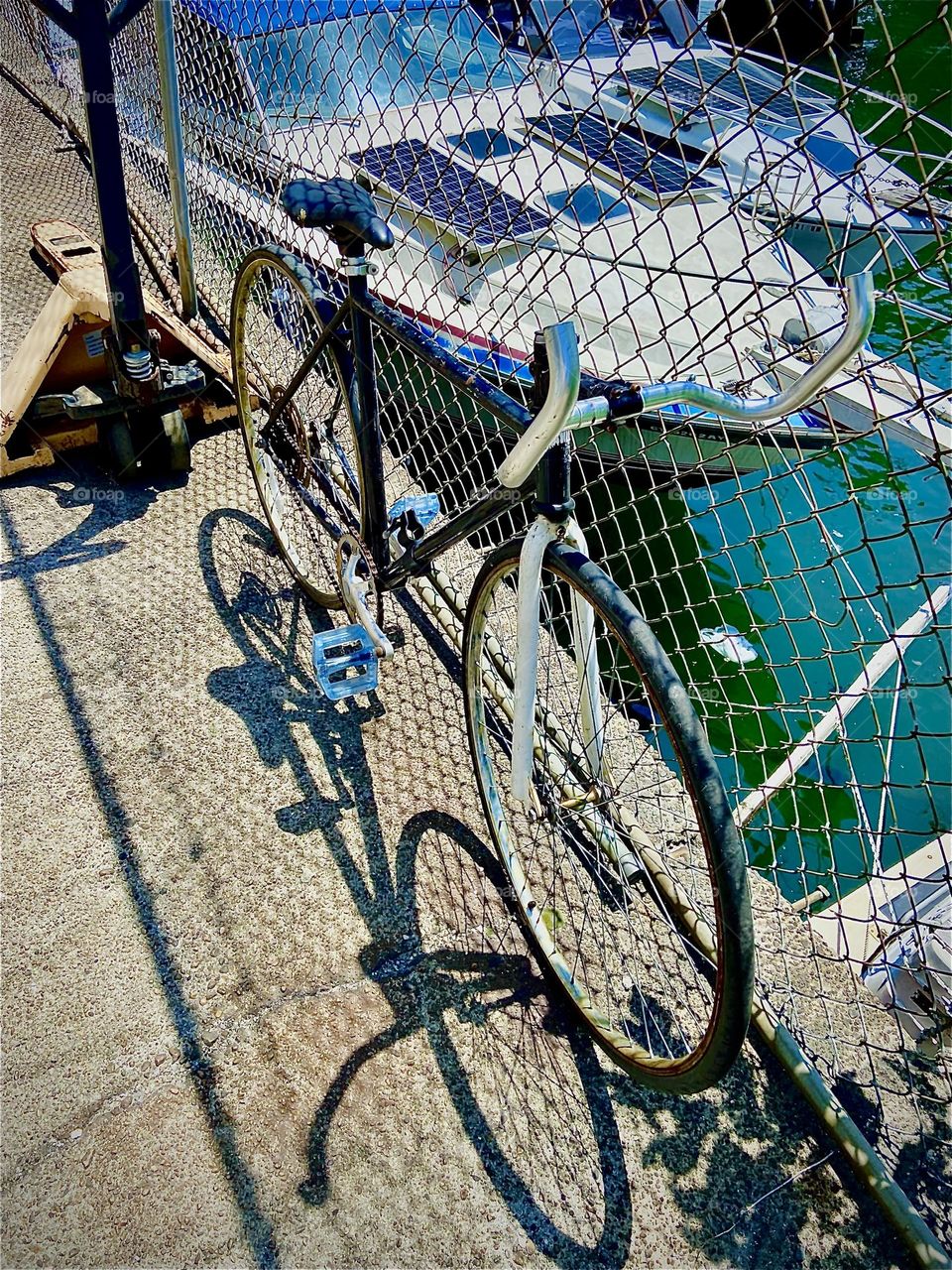 The ten speed bicycle is leaning against the metal mesh fence in an old building off „Borden Ave“ by the „Pulaski Bridge“ and „Newtown Creek“. Through the fence one can see the „East River“ and parts of various boats. 2022. Hypnotic Productions