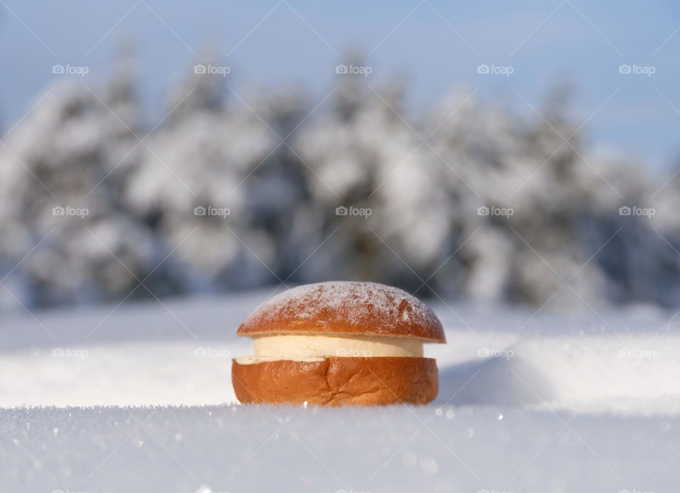 Traditional Finnish pre-Easter bun or lent bun filled with cream and almond paste and powdered sugar on top in deep fresh snow in winter forest.