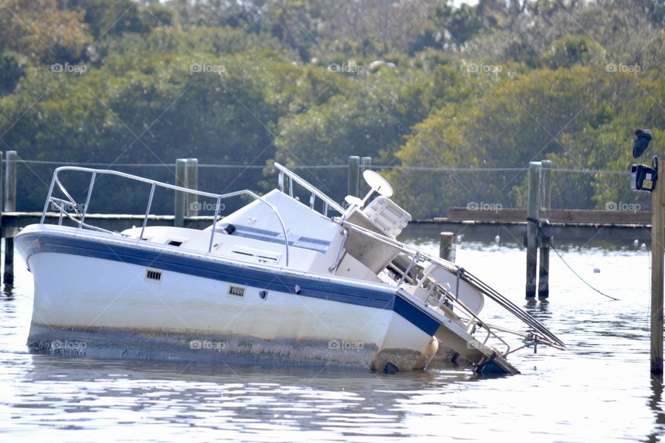 A white sailboat with a blue stripe sinking into river water near a dock