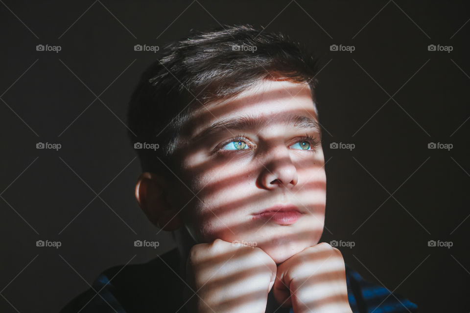 Close-up of thoughtful boy looking away against wall with sunlight falling on his face.