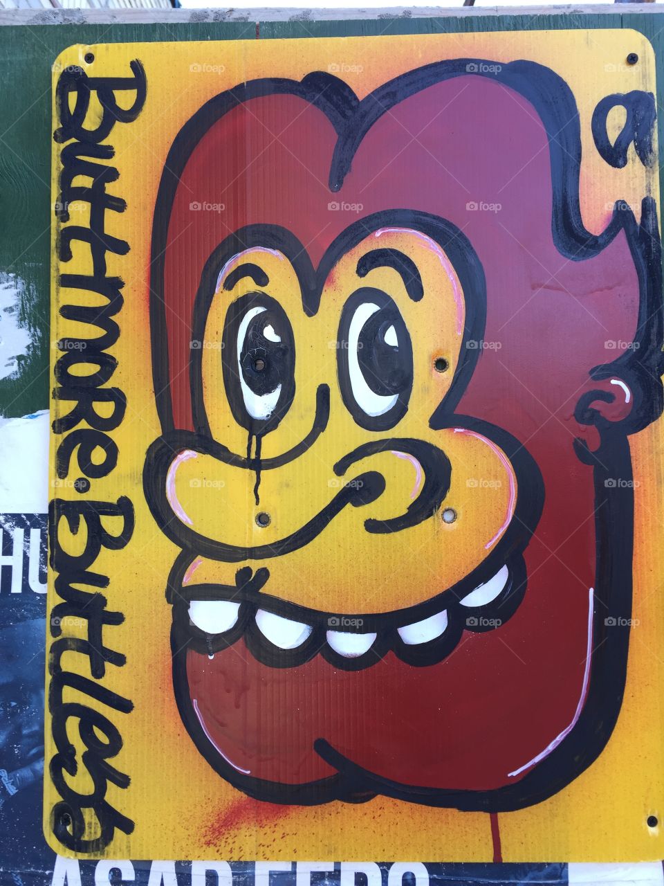 Photo of graffiti on construction site . Yellow and brown colors are used to depict the face of a lion or man face. The face is smiling. It depicts a retro urban art. the graffiti also depicts a monster . 