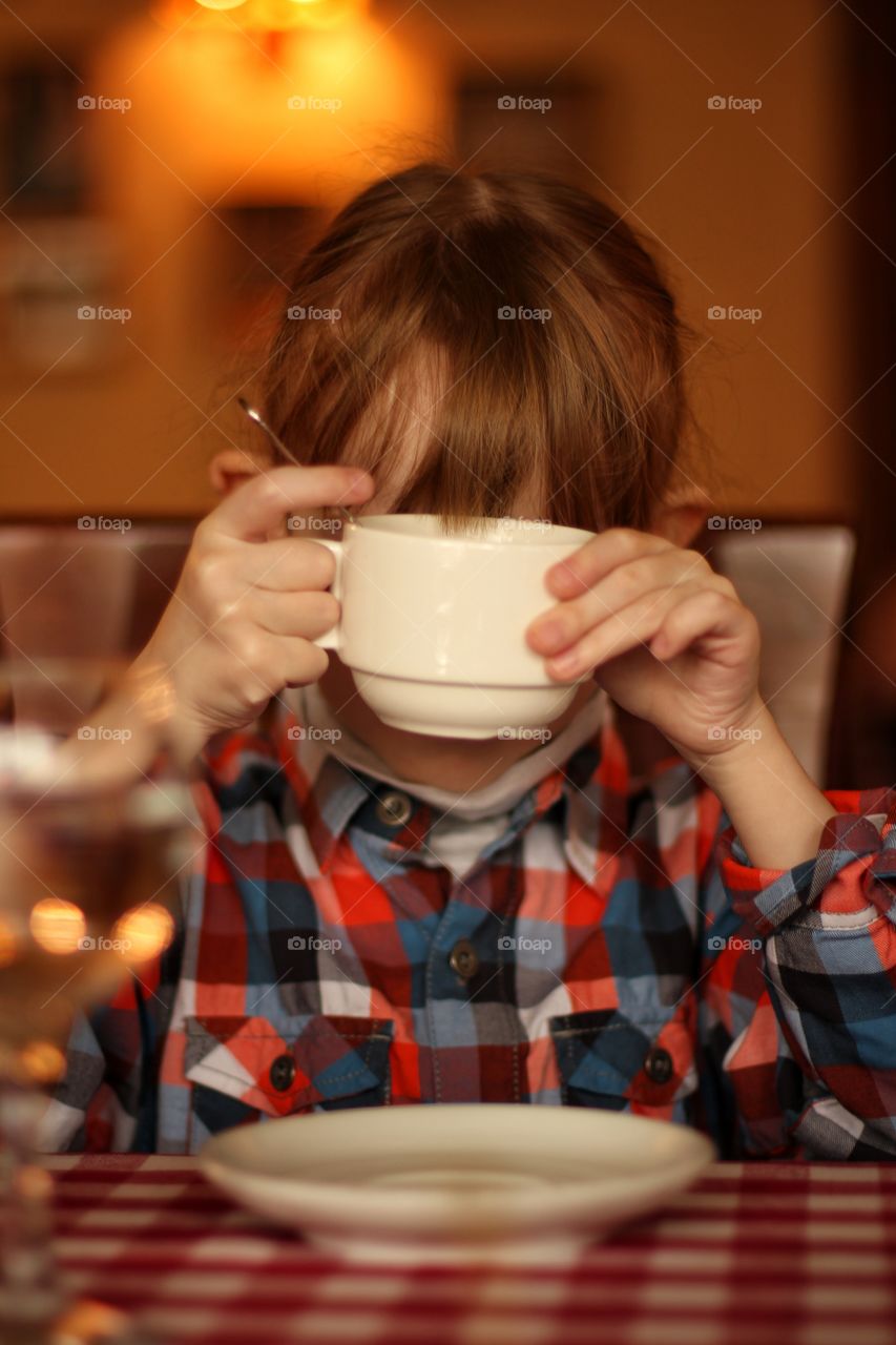 Little girl at the table hiding behind a white cup of tea