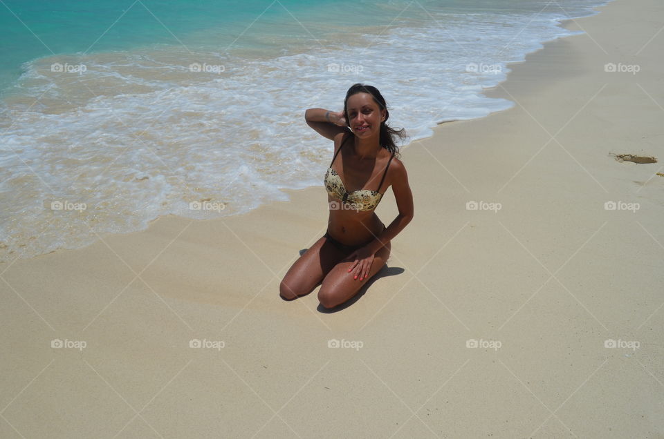 Girl in swimwear seating on the beach of blue sea on the white sand 