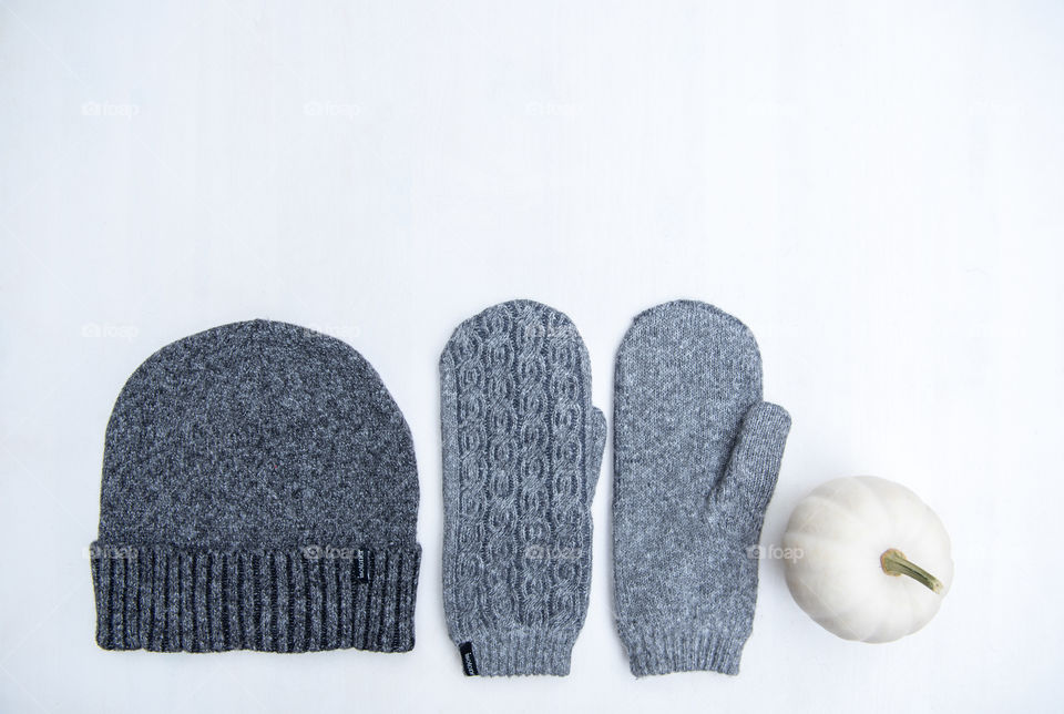 Flat lay of a pair of mittens and a beanie hat next to a white pumpkin