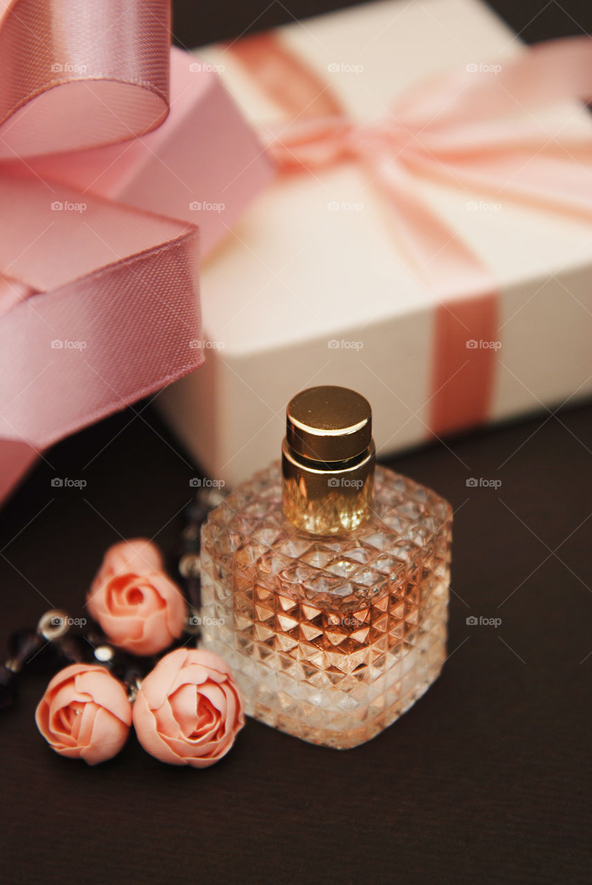 Perfume fragrance bottle. Women cosmetics gift boxes eith ribbon. Fake rosses. Dark background.