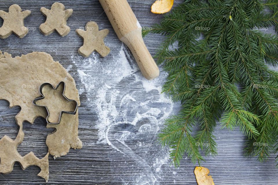 Cooking Christmas gingerbread cookies on a wooden table with tangerines and green Christmas trees.