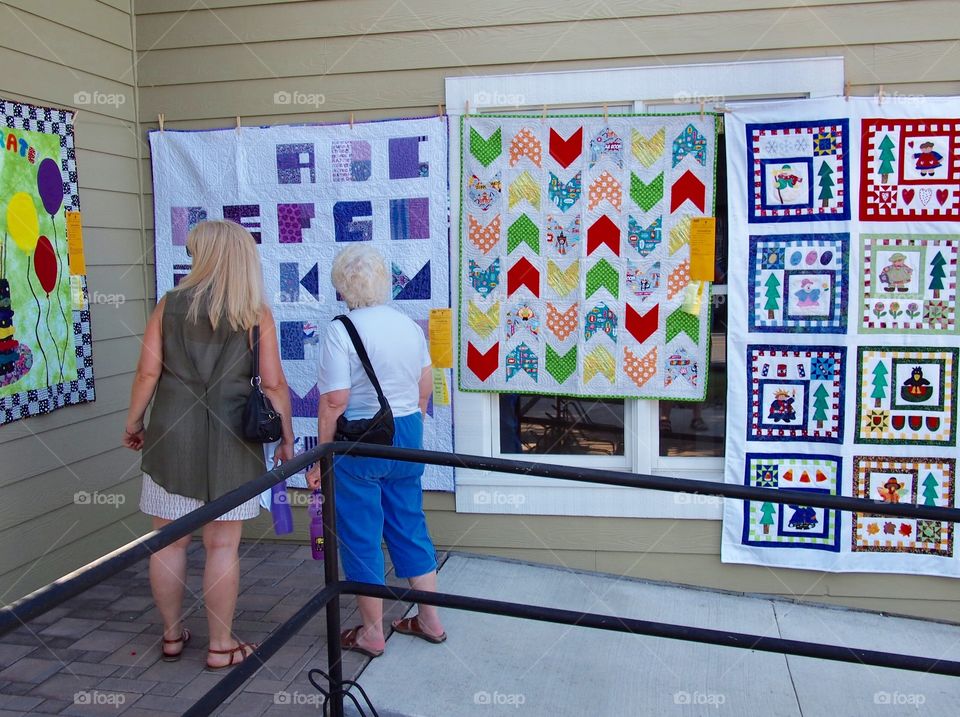 Two woman view with appreciation a row of beautiful quilts at the Annual Sisters Quilt Show in Central Oregon on a sunny summer day in July.