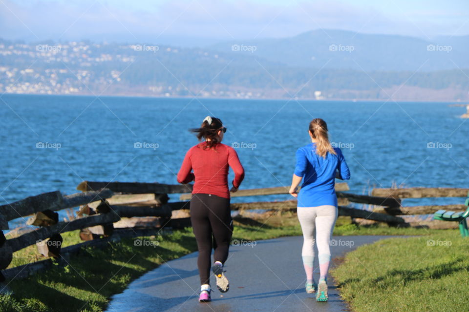 Young women running on the path by the coast on a sunny early spring day