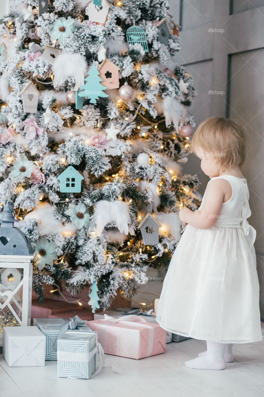 little girl decorates a Christmas tree with Christmas toys