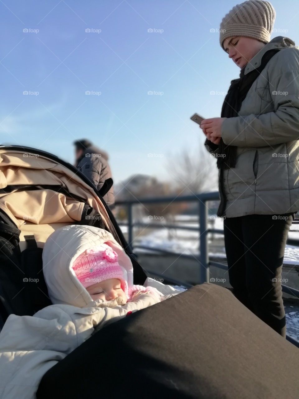 Baby girl napping in a stroller, mom checking her phone.