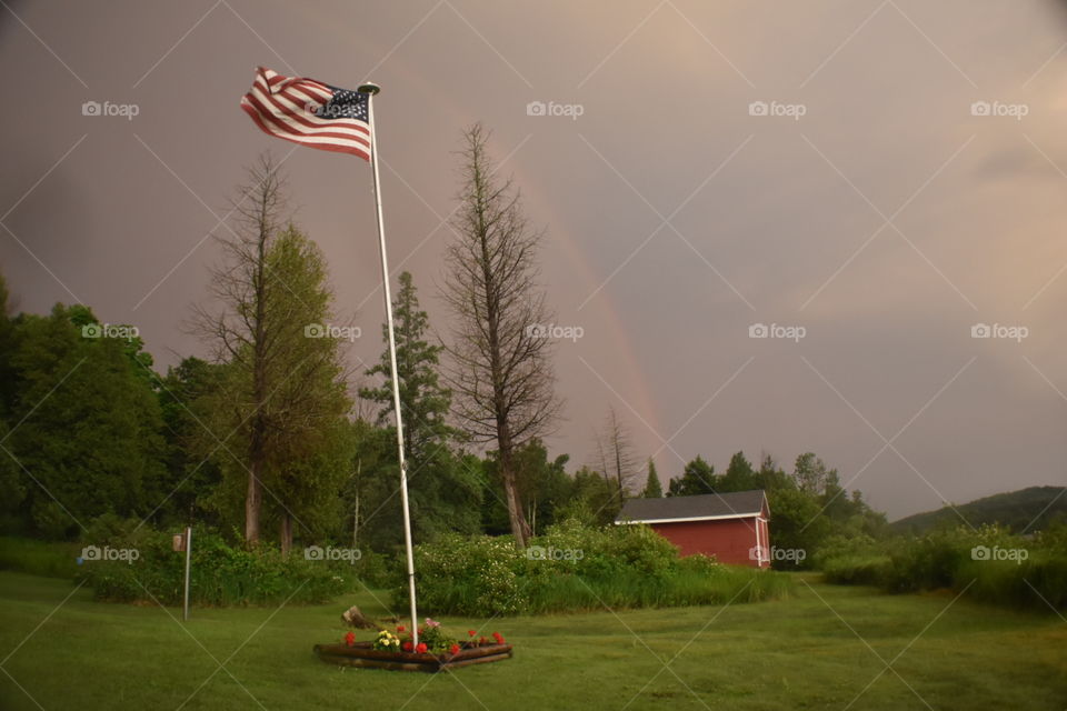 American flag against a dark cloudy backdrop with a faint rainbow