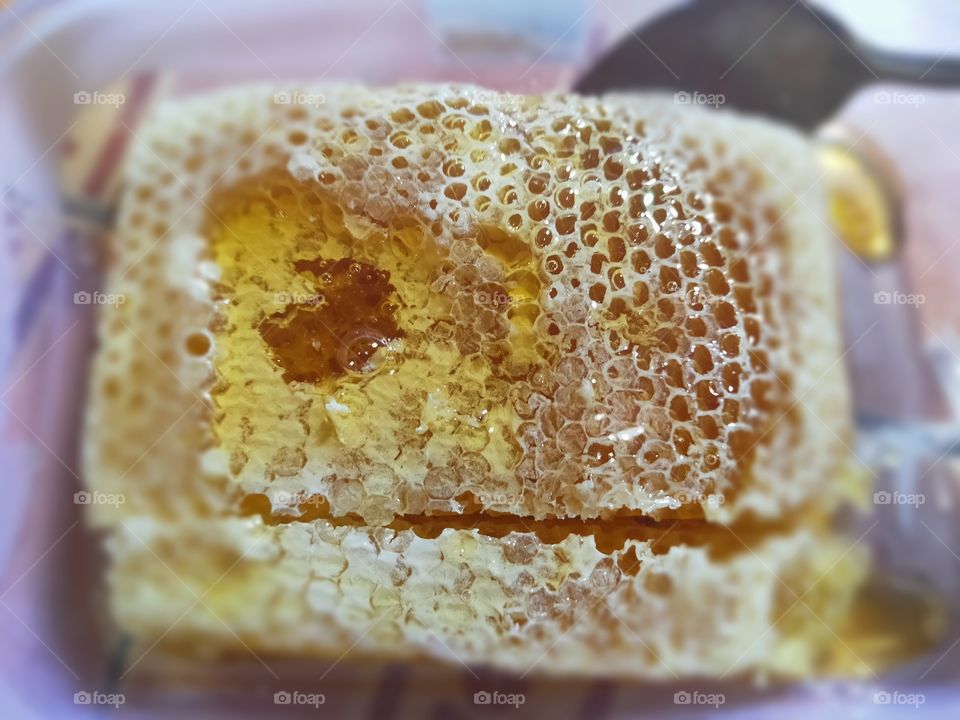 bee honey with its sarag for consumption. with a stainless spoon in the back