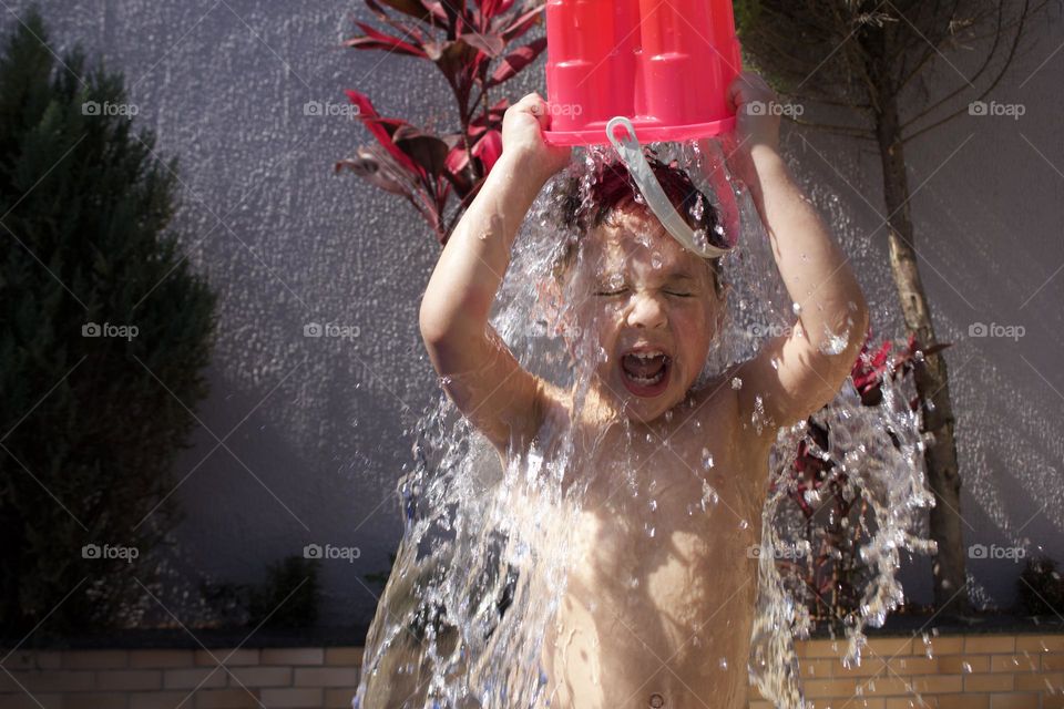 child getting wet with bucket of water on a hot summer day.