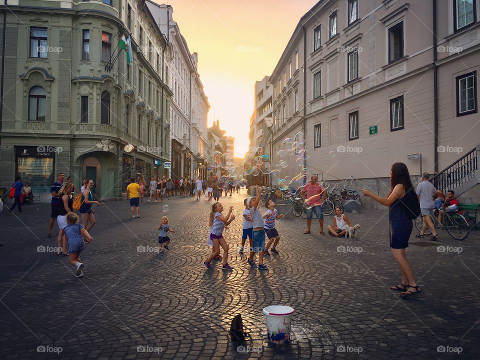 sunset on old town square of ljubljana, slovenia; children play with bubble under sunset
