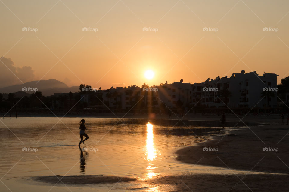 Sunset on the beach, silhouette of woman running in the sunlight reflection 