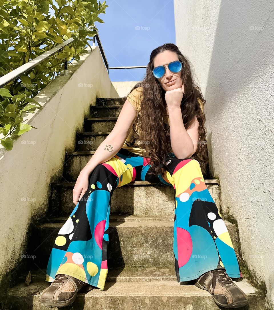 Woman in blue sunglasses and psychedelic flares sits on some steps