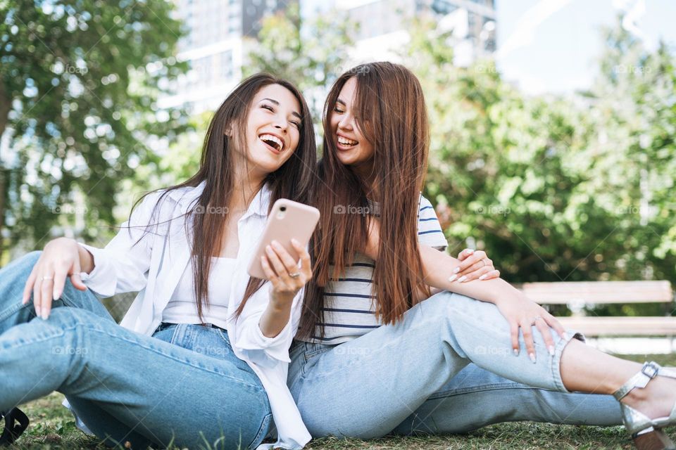 Young asian girls friends using mobile phone having fun in city park
