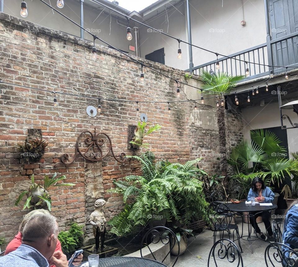 charming outdoor cafe patio with exposed brick, string lights, bistro tables and live plants throughout