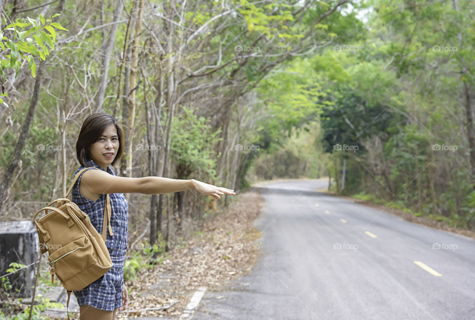 Women raise their arm waving car on the road with the tree cover.