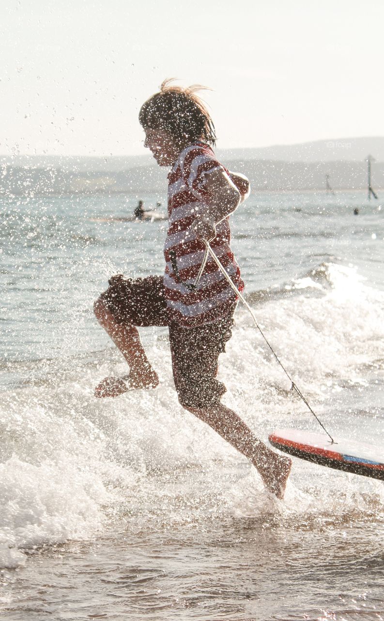 Bodyboarding excitement . Excited child jumping into the sea with his bodyboard