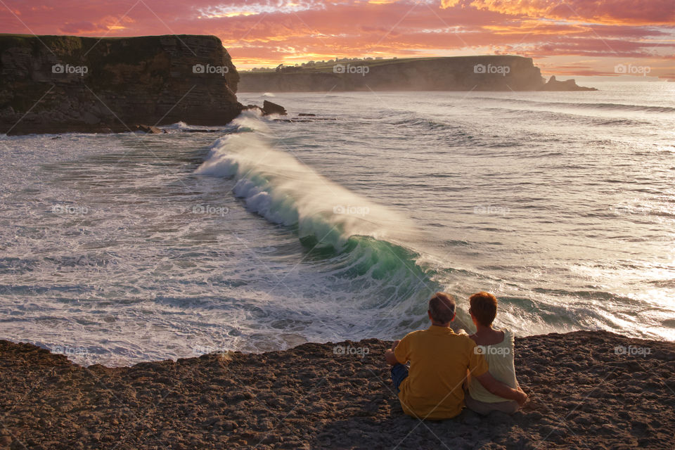 Couple of lovers sitting in front of the sea at sunset 