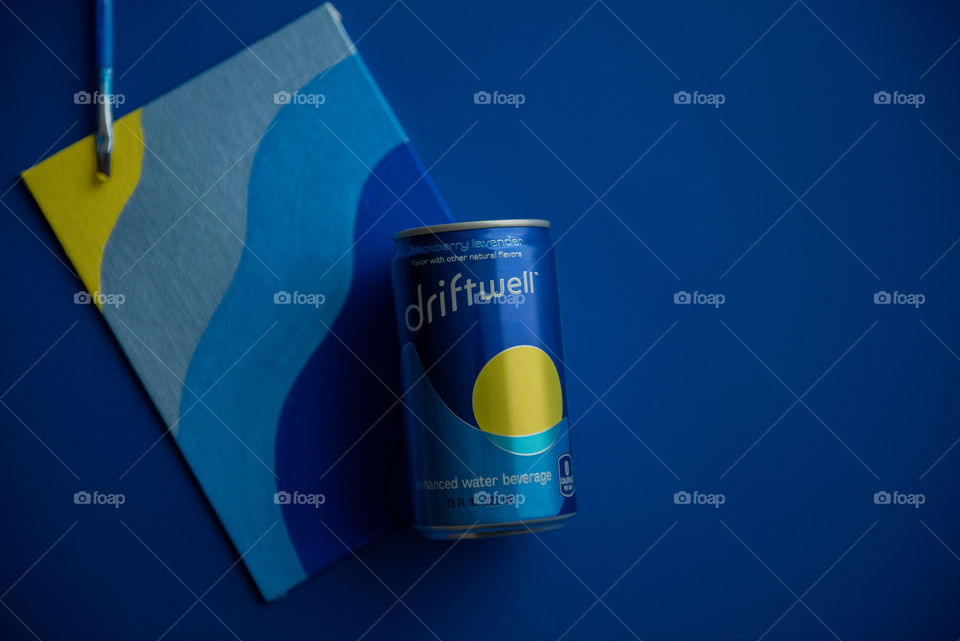 Monochromatic flat lay of a can of Driftwell on blue background with a blue painting