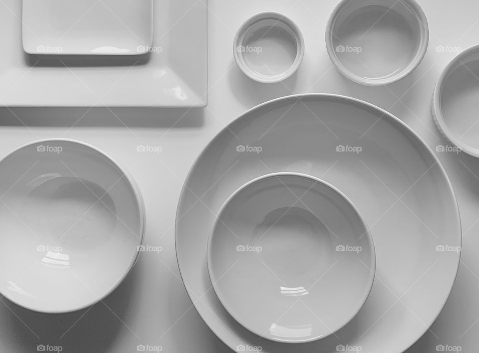 Assortment of white plates and bowls on a white table.