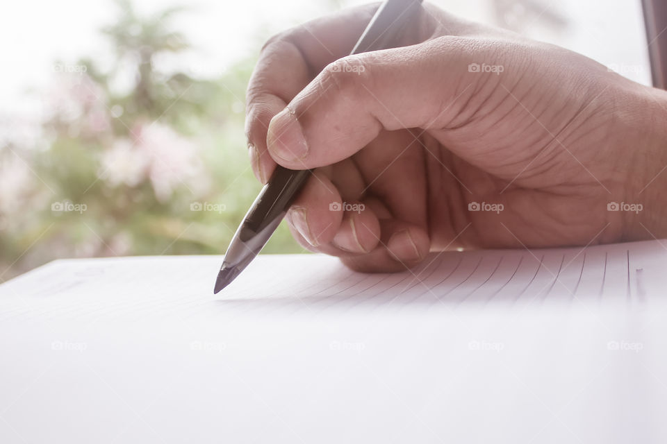 Closeup of man's hand working on a sheet of paper document with pen at desk. A businessman working on a financial report. Loan Tax Vat computation background concept. Copy space room for text.