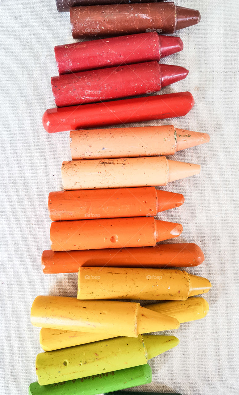 Children crayons aligned in rainbow colors in a line on a table ; brown, red, bordeaux, beige, orange, yellow, dark and light green