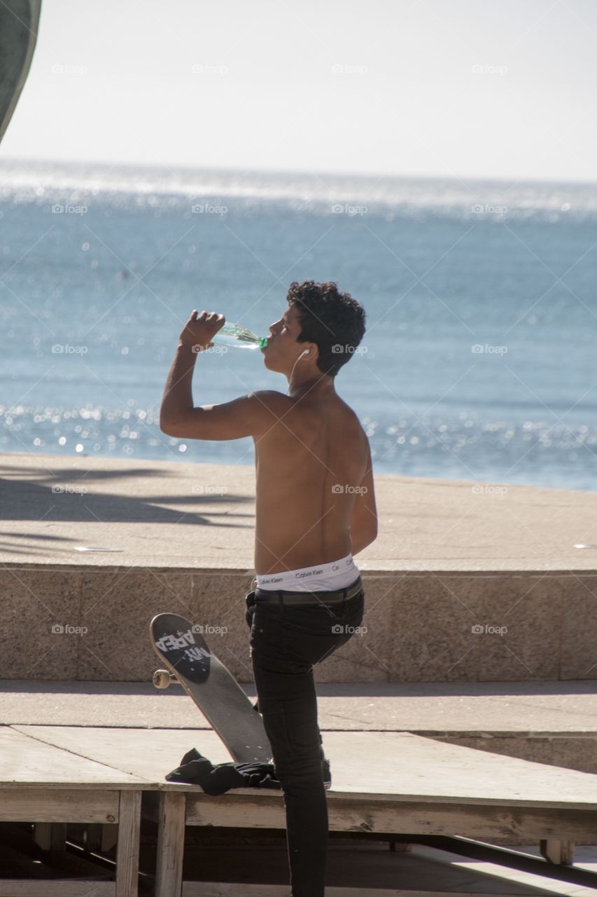 A guy with his skateboard in the burning sum of spain takes time for a refreshment