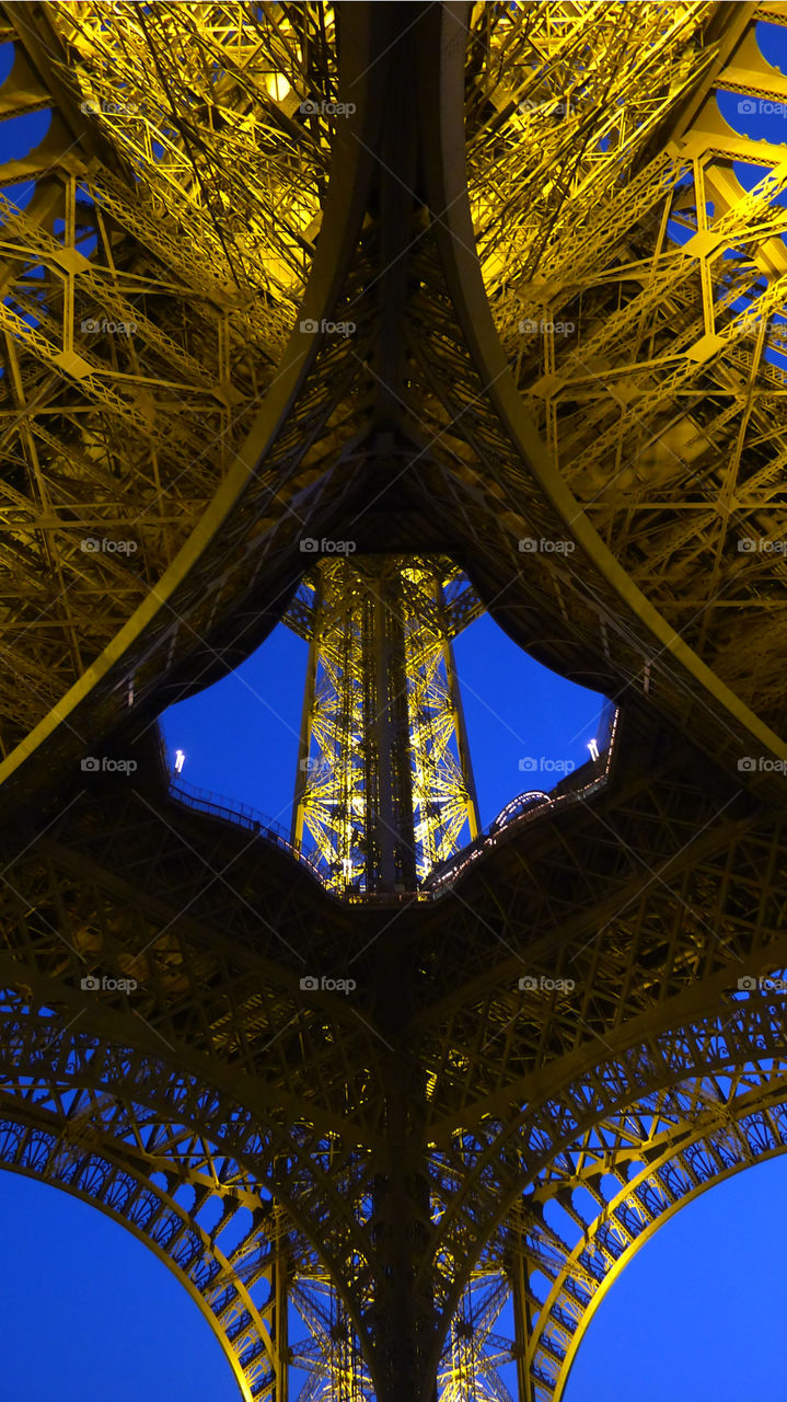 Abstract view of the Eiffel tower against a clear blue night sky. Taken from directly below.