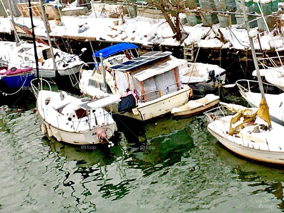 A view of Newtown Creek in Long Island City, Queens, NY and its multiple boats of all different kinds by the shore that is at this time of year covered in at least a foot of bright white snow. 2020. Hypnotic Productions