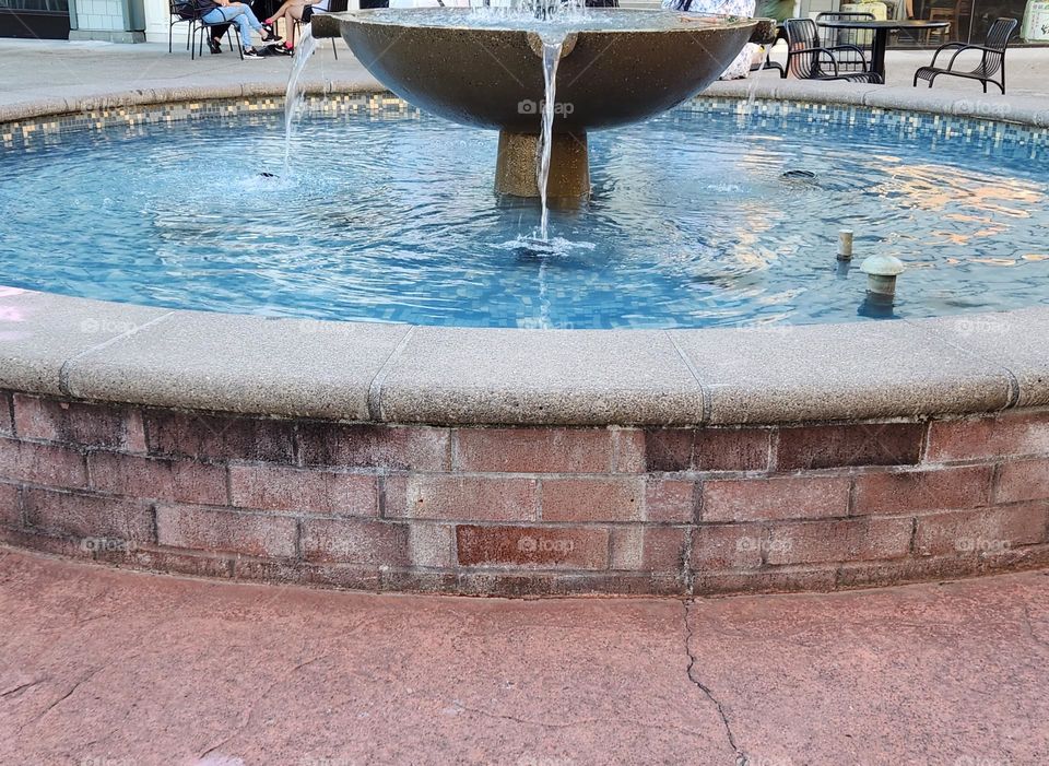 bright blue water pouring down into a brick walled outdoor shopping center court fountain on a warm Summer evening in Oregon