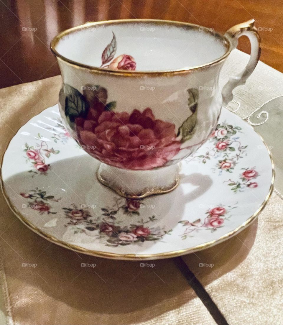 The classic tea cup and matching plate feature a delicate pink floral design, adding a soft, vintage charm. The tea cup and plate are highlighted by delicate, shiny gold bands. Together, the set presents a timeless and graceful aesthetic.