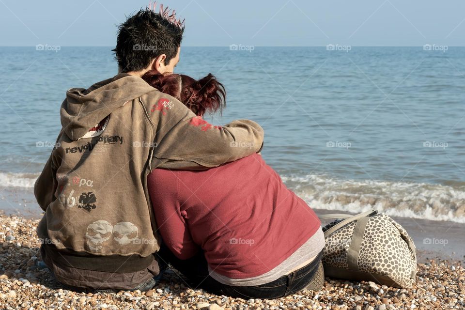 Young couple hug on the beach as they look out to sea