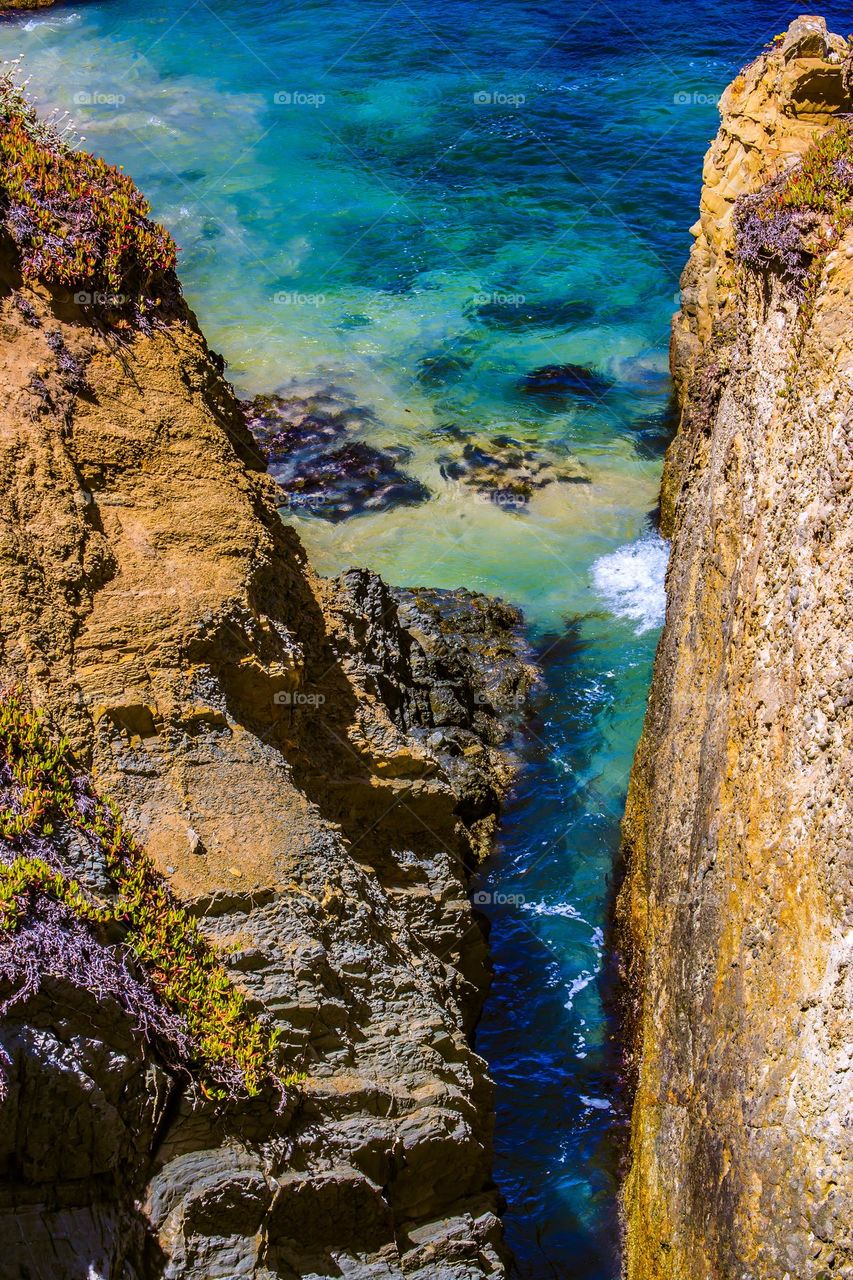 View between the cliffs at the pigeon point lighthouse off highway one between San Francisco and Santa Cruz in California. The water is clear on a sunny day off the pacific coast.