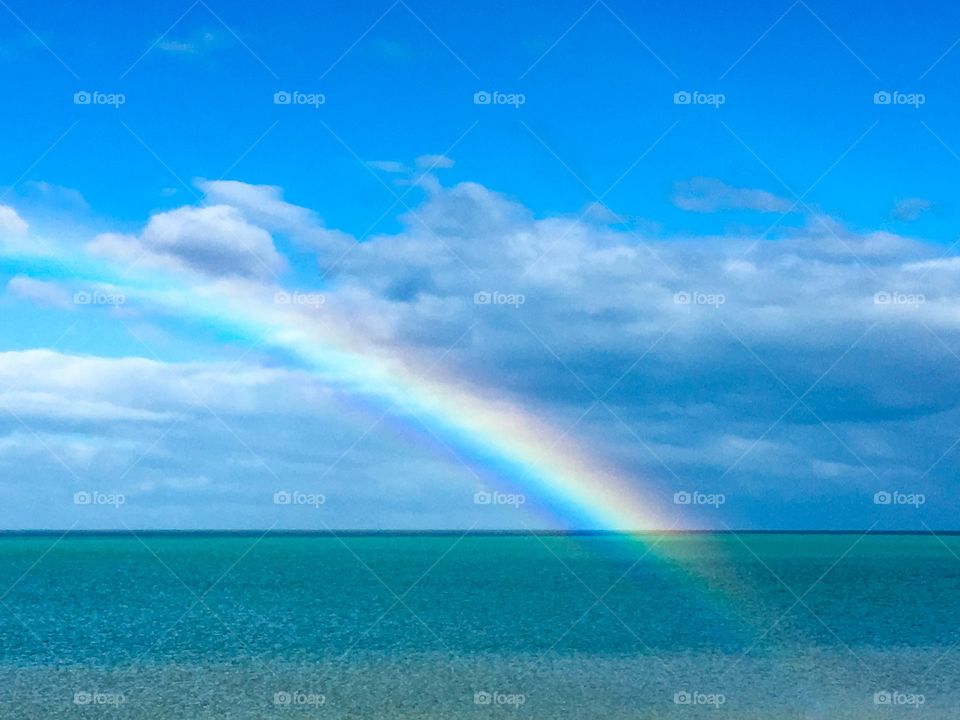 Bright colourful rainbow over the ocean, end of rainbow illuminating water